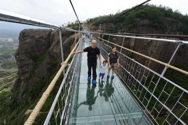 PINGJIANG, CHINA - SEPTEMBER 24: (CHINA OUT) Tourists walk on a suspension bridge made of glass at the Shiniuzhai National Geological Park on September 24, 2015 in Pingjiang County, China. The 300-meter-long glass suspension bridge, with a maximum height of 180 meters, opened to the public on Thursday. (Photo by ChinaFotoPress/ChinaFotoPress via Getty Images)